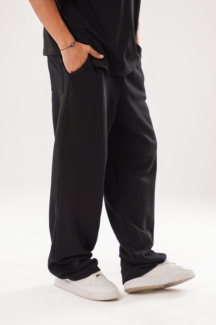 A person wearing casual black lounge pants paired with stylish white sneakers on a plain background.