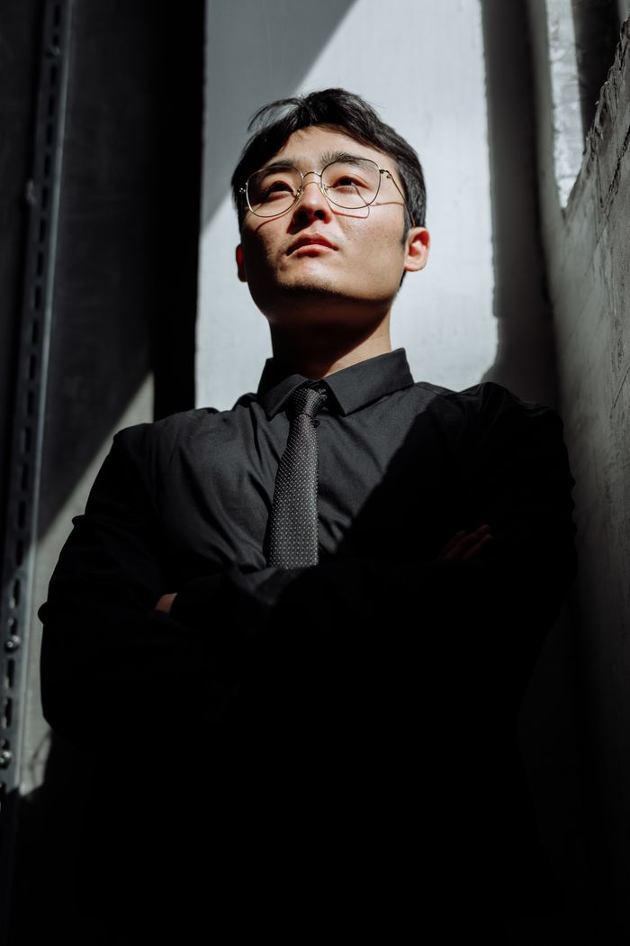Portrait of an Asian man in black corporate attire, exuding confidence in a dramatic light setting.