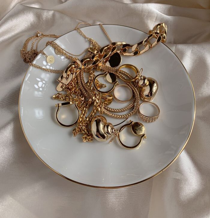 Stylish gold rings and necklaces elegantly displayed on a saucer with a silk background.